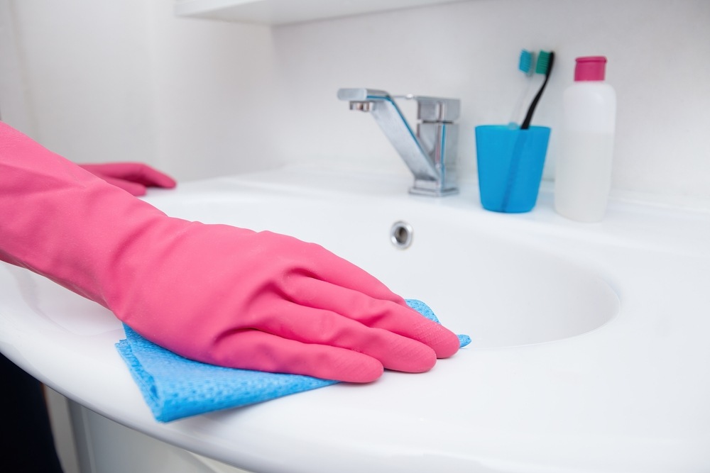 Person-reinigt-Waschbecken-und-Wasserhahn