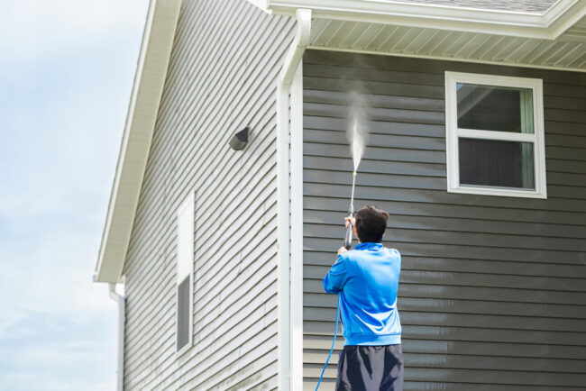 Mann-reinigt-mit-Hochdruckdüse-die-Aussenfassade Mann-reinigt-mit-Hochdruckdüse-die-Aussenfassade