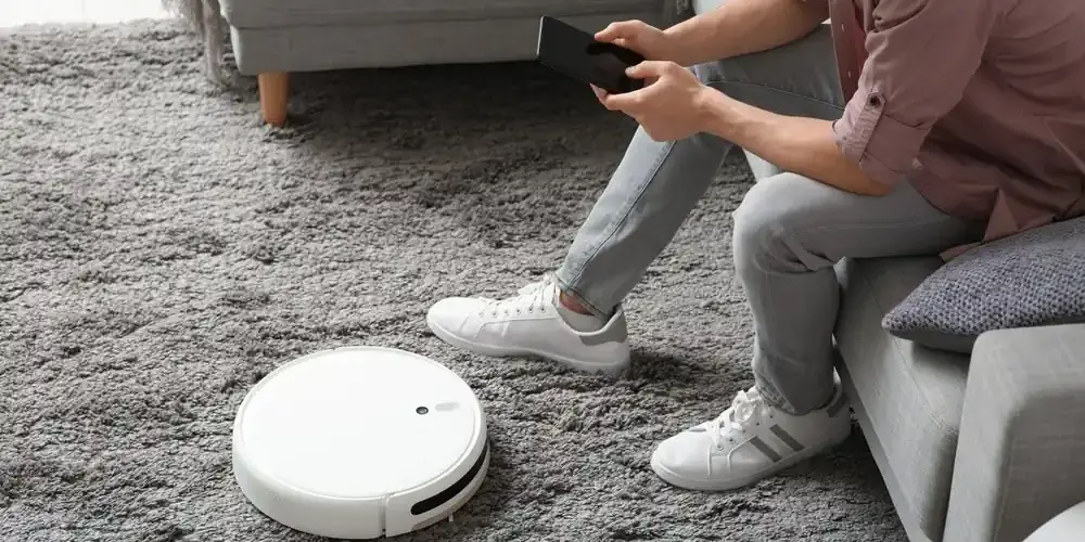 Mann mit Mobiltelefon und modernem Roboterstaubsauger Mann mit Mobiltelefon und modernem Roboterstaubsauger